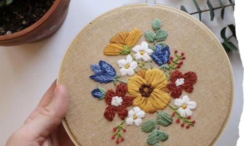 colorful embroidered flowers on tan cloth in round embroidery hoop