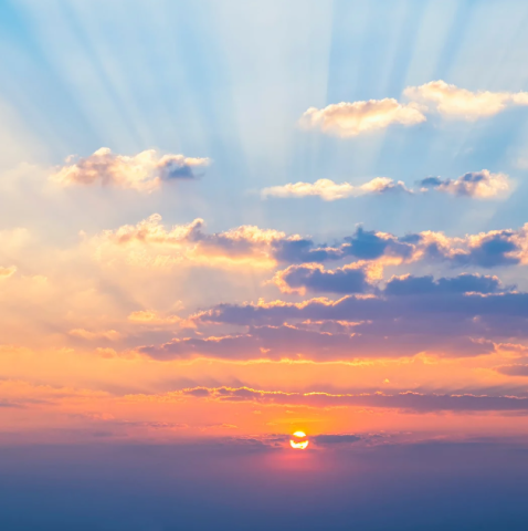 a beautiful sunset with purples, oranges, yellows and blues with puffy white clouds and sunrays piercing through the clouds