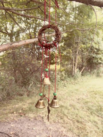 a wooden wreath with bells and charms hanging from it with a tree in the background