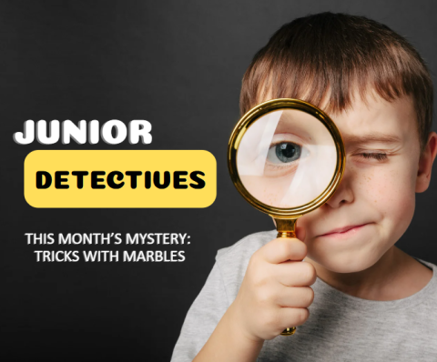 Bold words "Junior Detective" in the top left corner with the words "this month’s mystery: Tricks with marbles" beneath it. The rest of the image is of a young boy holding a magnifying glass to his eye.