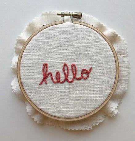 The word hello hand embroidered in red on cream fabric.