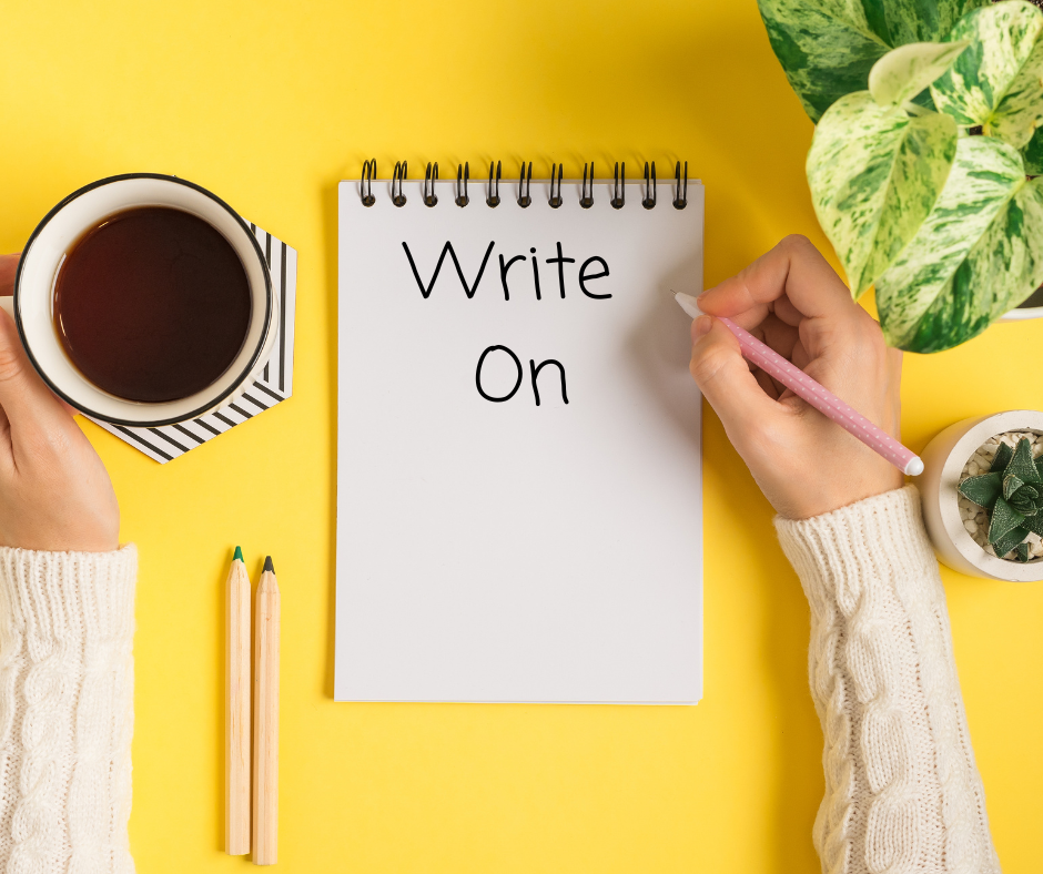 Yellow background with coffee mug, green plant, notebook, pen, and a hand writing.