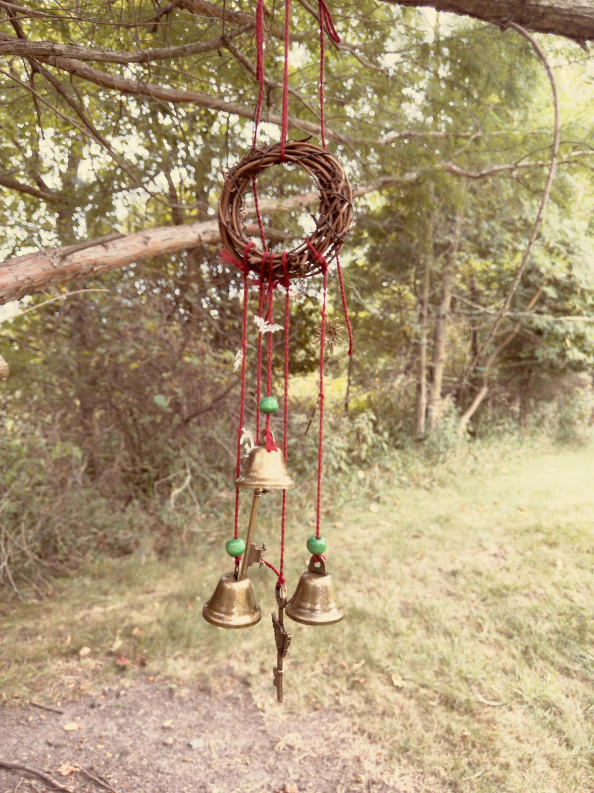 a wooden wreath with bells and charms hanging from it with a tree in the background